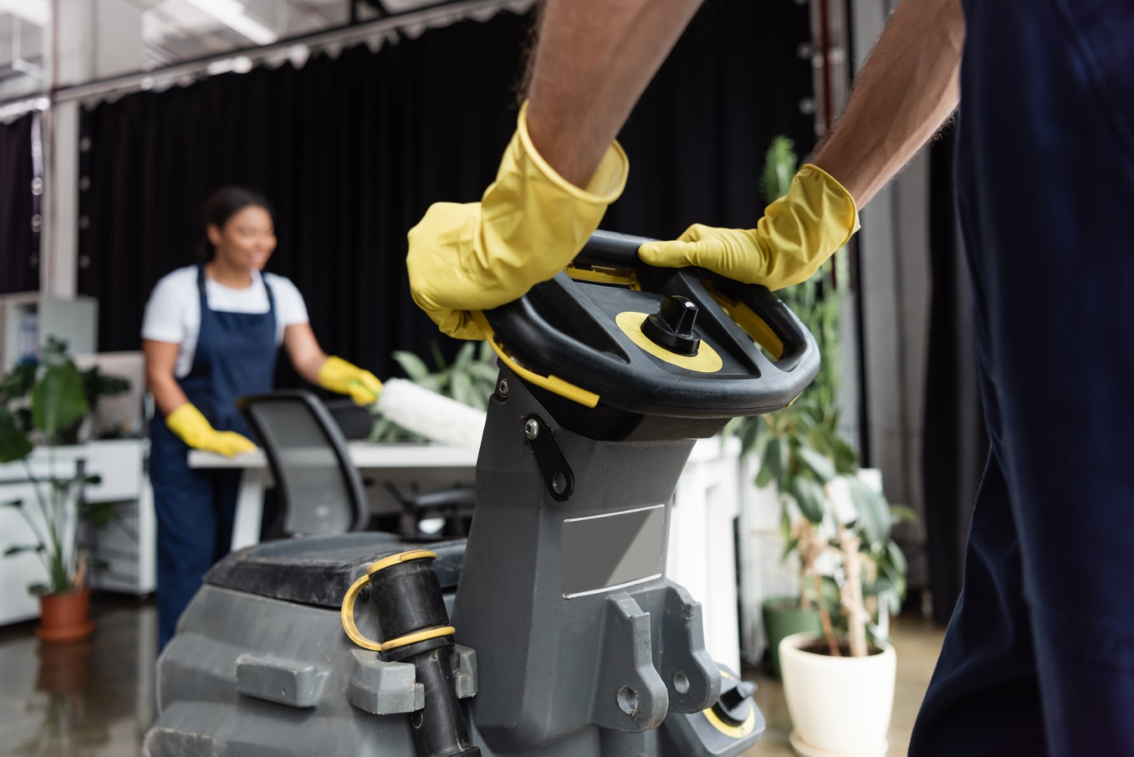 cropped view of man in rubber gloves operating floor scrubber machine near blurred bi-racial woman
